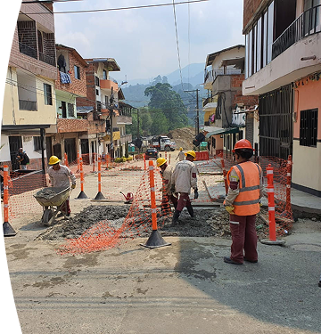 Trabajadores de construcción con cascos y uniformes de seguridad realizan obras en una calle residencial, rodeados de mallas naranjas de protección.