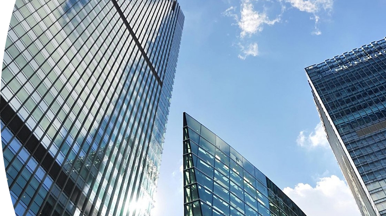 Vista desde abajo de varios edificios modernos de vidrio y acero reflejando el cielo azul con algunas nubes
