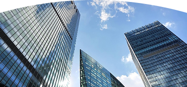 Vista desde abajo de varios edificios modernos de vidrio y acero reflejando el cielo azul con algunas nubes