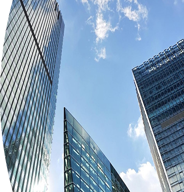 Vista desde abajo de varios edificios modernos de vidrio y acero reflejando el cielo azul con algunas nubes