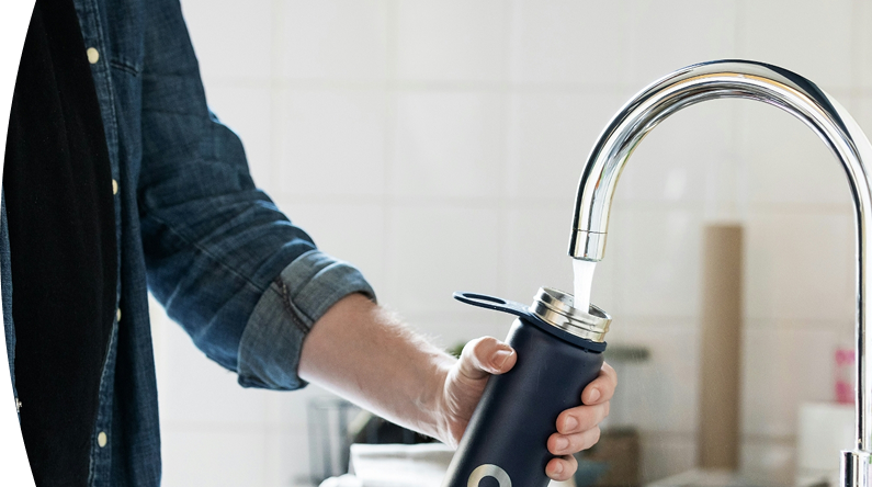 Persona llenando un termo negro con agua en una canilla