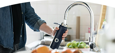 Persona llenando un termo negro con agua en una canilla