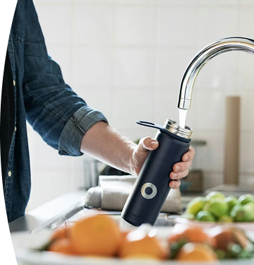 Persona llenando un termo negro con agua en una canilla