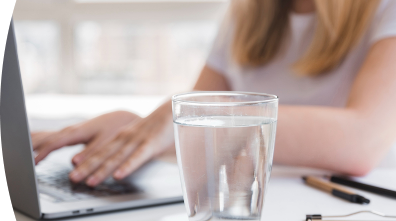 Banner con título "Indicadores de Calidad" acompañado de una imagen de un vaso con agua sobre una mesa y de fondo unas manos de una persona trabajando en su computador