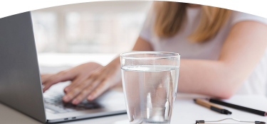 Banner con título "Indicadores de Calidad" acompañado de una imagen de un vaso con agua sobre una mesa y de fondo unas manos de una persona trabajando en su computador