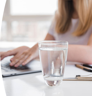 Banner con título "Indicadores de Calidad" acompañado de una imagen de un vaso con agua sobre una mesa y de fondo unas manos de una persona trabajando en su computador