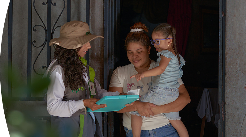 Mujer sosteniendo a una niña en brazos mientras conversa con una trabajadora de EPM