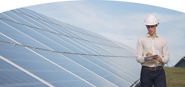 Ingeniero con casco inspeccionando y tomando notas frente a paneles solares en una planta de energía solar