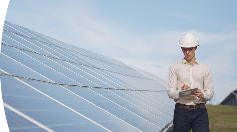 Ingeniero con casco inspeccionando y tomando notas frente a paneles solares en una planta de energía solar
