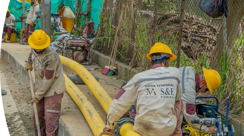 Operarios con cascos amarillos y uniformes de contratista de EPM trabajan en la instalación de tuberías amarillas de gas natural en una acera.