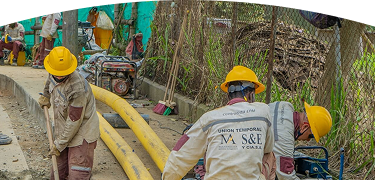 Operarios con cascos amarillos y uniformes de contratista de EPM trabajan en la instalación de tuberías amarillas de gas natural en una acera.