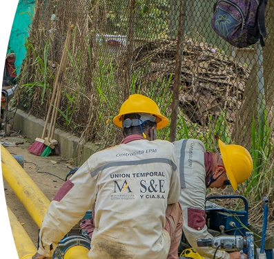 Operarios con cascos amarillos y uniformes de contratista de EPM trabajan en la instalación de tuberías amarillas de gas natural en una acera.