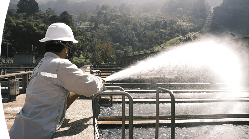 Trabajador de EPM opera equipo en una planta de tratamiento de agua rodeada de naturaleza.