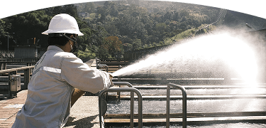 Trabajador de EPM opera equipo en una planta de tratamiento de agua rodeada de naturaleza.