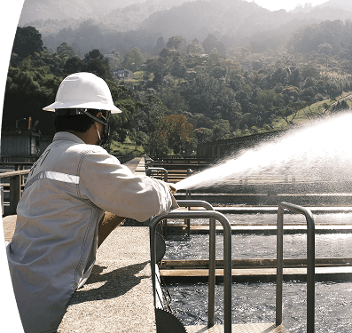Trabajador de EPM opera equipo en una planta de tratamiento de agua rodeada de naturaleza.