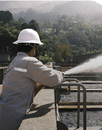 Trabajador de EPM opera equipo en una planta de tratamiento de agua rodeada de naturaleza.