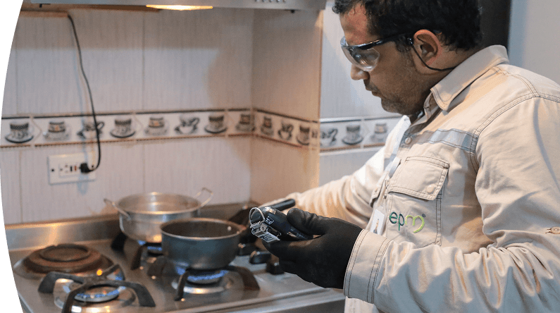 Técnico de EPM revisa un medidor de gas en una cocina mientras la estufa está encendida.