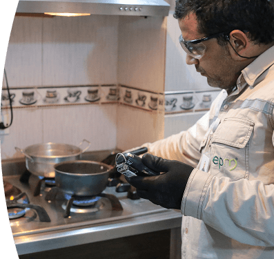 Técnico de EPM revisa un medidor de gas en una cocina mientras la estufa está encendida.