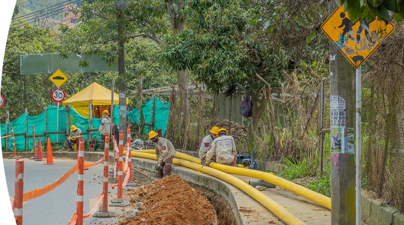 Operarios con cascos amarillos y uniformes de contratista de EPM trabajan en la instalación de tuberías amarillas de gas natural en una acera.