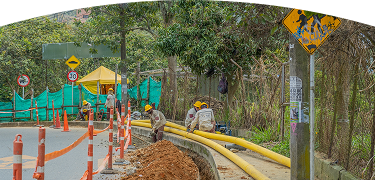 Operarios con cascos amarillos y uniformes de contratista de EPM trabajan en la instalación de tuberías amarillas de gas natural en una acera.