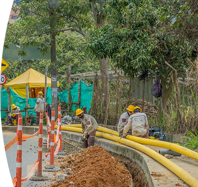 Operarios con cascos amarillos y uniformes de contratista de EPM trabajan en la instalación de tuberías amarillas de gas natural en una acera.