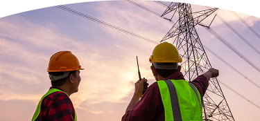 Banner "Energía constructor y urbanizador" con imagen de dos trabajadores con cascos y chalecos reflectantes observan y señalan una torre electrica al atardecer