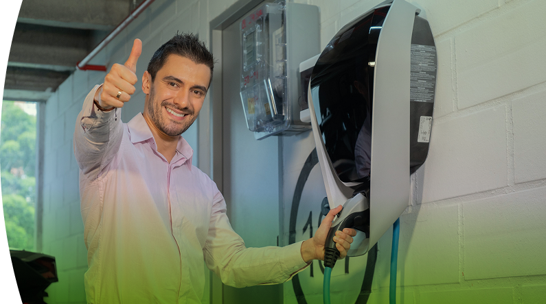 Hombre sonriente conectando su carro eléctrico en una estación de carga instalada en un parqueadero cubierto