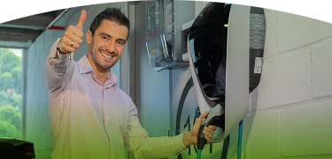 Hombre sonriente conectando su carro eléctrico en una estación de carga instalada en un parqueadero cubierto
