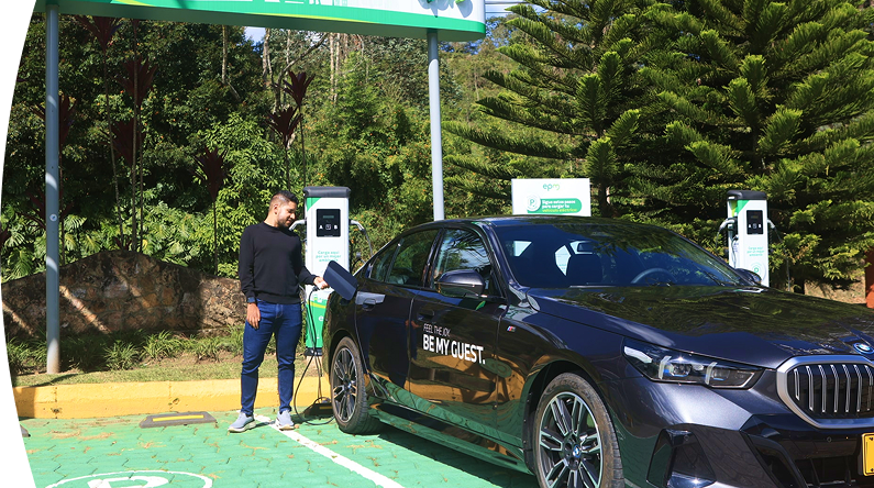 Banner ''Carga pública'' acompañado de un hombre conectando un carro eléctrico BMW en una estación de carga pública de EPM, rodeada de vegetación