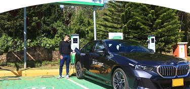 Banner ''Carga pública'' acompañado de un hombre conectando un carro eléctrico BMW en una estación de carga pública de EPM, rodeada de vegetación