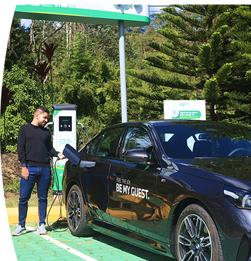 Banner ''Carga pública'' acompañado de un hombre conectando un carro eléctrico BMW en una estación de carga pública de EPM, rodeada de vegetación