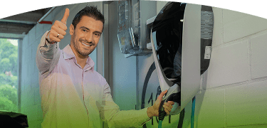 Hombre sonriente conectando su carro eléctrico en una estación de carga instalada en un parqueadero cubierto