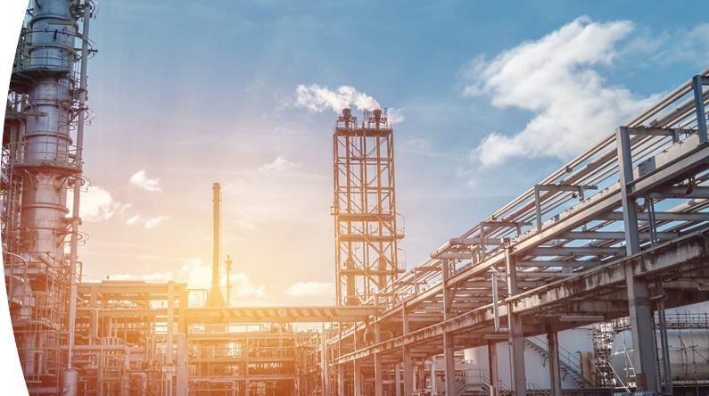 Planta industrial con chimeneas y tuberías, emitiendo vapor o humo bajo un cielo azul con nubes y un sol brillante