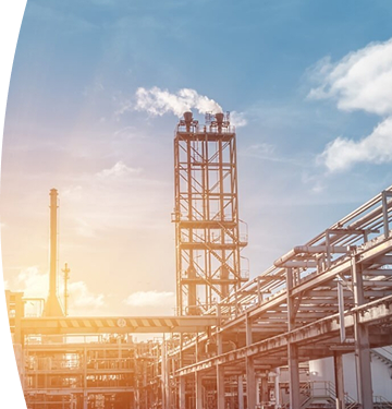 Planta industrial con chimeneas y tuberías, emitiendo vapor o humo bajo un cielo azul con nubes y un sol brillante