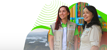 Dos colaboradoras de EPM sonríen durante una visita comunitaria en zona rural, con paisaje montañoso y arquitectura colorida de fondo