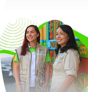 Dos colaboradoras de EPM sonríen durante una visita comunitaria en zona rural, con paisaje montañoso y arquitectura colorida de fondo