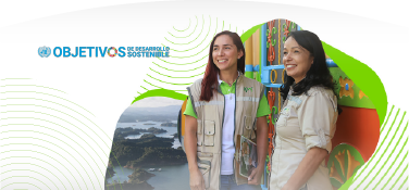 Dos colaboradoras de EPM sonríen durante una visita comunitaria en zona rural, con paisaje montañoso y arquitectura colorida de fondo