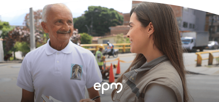 Colaboradora de EPM conversa con un adulto mayor mientras registra información en una tabla durante visita comunitaria.