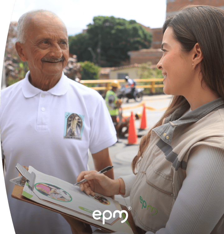 Colaboradora de EPM conversa con un adulto mayor mientras registra información en una tabla durante visita comunitaria.