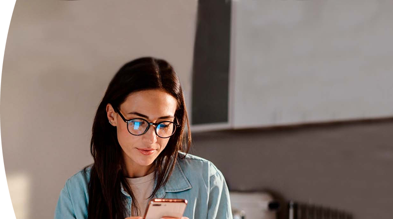 mujer con gafas y chaqueta de mezclilla observando la pantalla de su teléfono móvil con atención