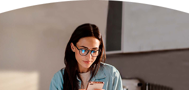 mujer con gafas y chaqueta de mezclilla observando la pantalla de su teléfono móvil con atención