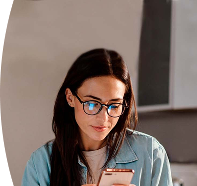 mujer con gafas y chaqueta de mezclilla observando la pantalla de su teléfono móvil con atención