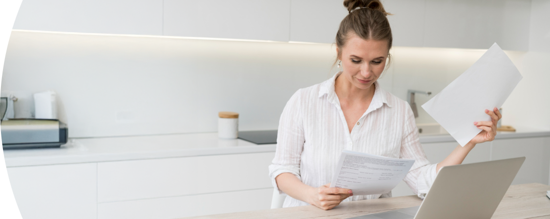 Mujer en la cocina revisa documentos en una laptop