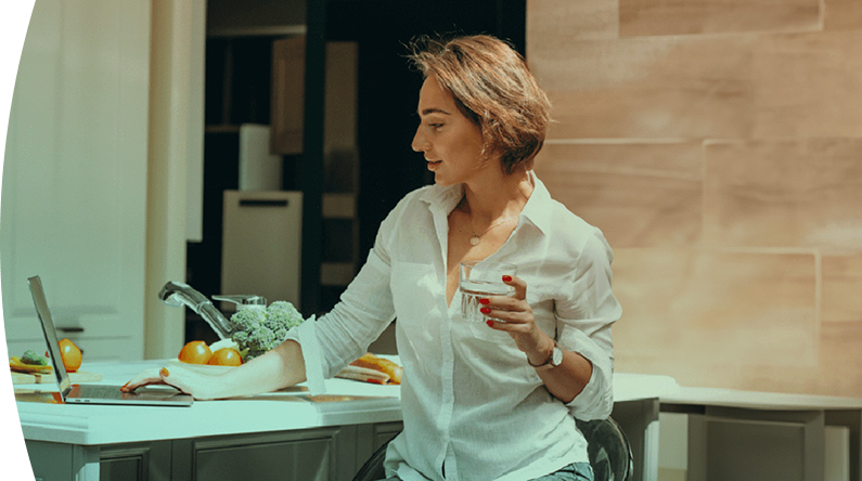 mujer en la cocina de su casa, tiene un vaso de agua en la mano 