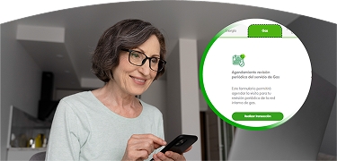 Mujer mayor con gafas, usando su celular frente al portátil, gestionando un servicio de EPM.