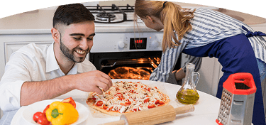 Hombre prepara una pizza mientras una mujer revisa el horno encendido en una cocina
