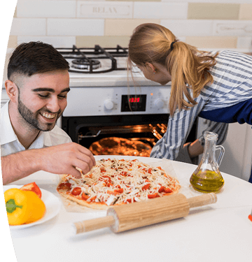 Hombre prepara una pizza mientras una mujer revisa el horno encendido en una cocina