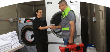 Técnico EPM y trabajadora se saludan frente a una lavadora industrial en un espacio de lavandería.