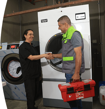 Técnico EPM y trabajadora se saludan frente a una lavadora industrial en un espacio de lavandería.