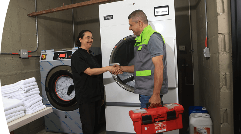 Técnico EPM y trabajadora se saludan frente a una lavadora industrial en un espacio de lavandería.